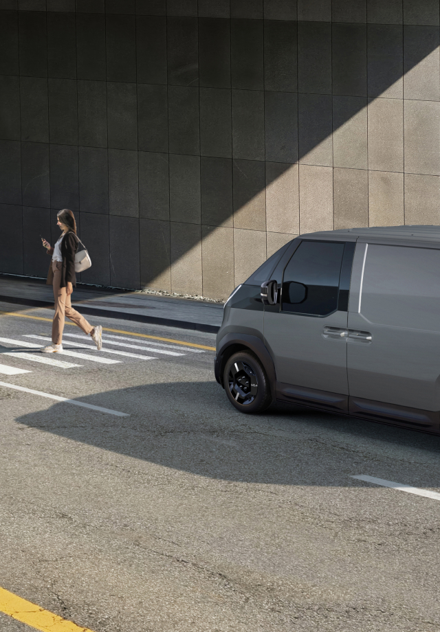Der Kia PV5 Cargo hält am Zebrastreifen, während ein Fußgänger vorbeigeht.